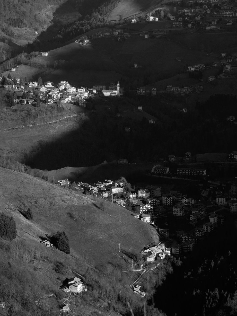 Zambla Alta e Zambla bassa viste dalla cima del monte Castello. Uno scatto in bianco e nero in cui l'ombra del monte Alben disegna una S lasciando illuminate chiese e chiesine dei paesi